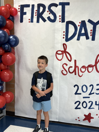 Student standing in front of first day of school sign 